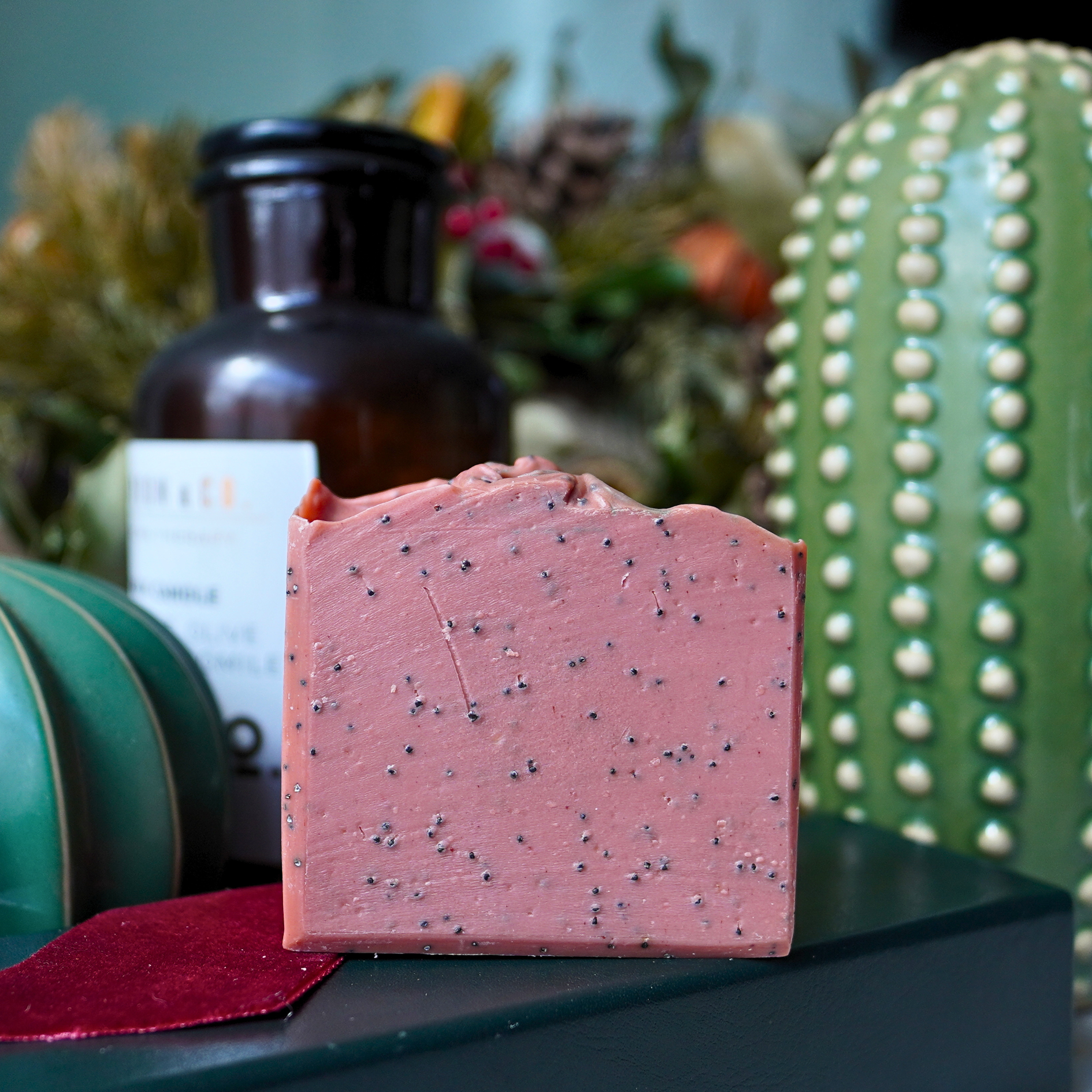 Pink speckled soap bar on a black surface with a cactus and bottle in the background